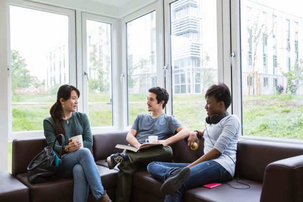 Three students sat on corner sofa together catching up